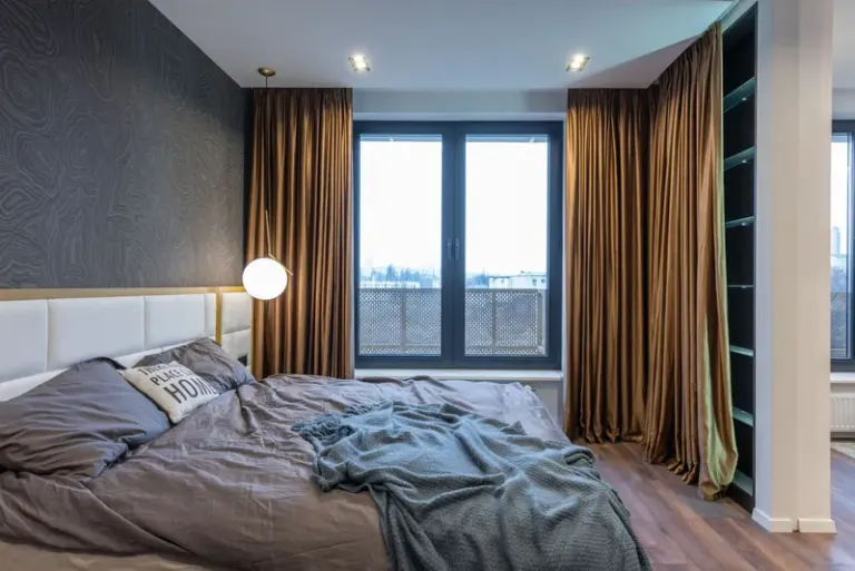 Interior of light modern flat with soft bed with pillows and blanket near lamp and window with curtains Stock Photo