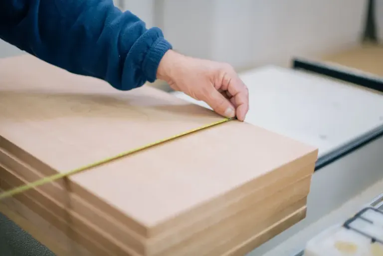Close-up of a carpenter's hand using a tape measure to measure wooden planks indoors. Stock Photo