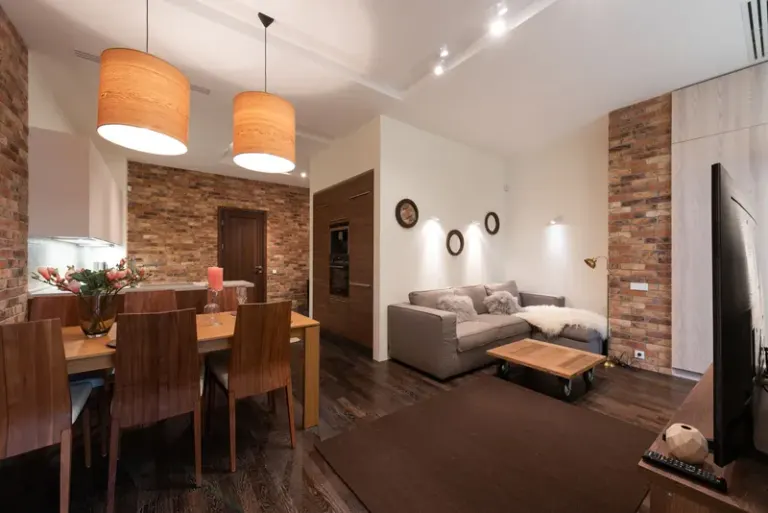 Modern apartment interior with dining table and chairs decorated with candles and flower vase with lamps on ceiling near cabinets and couch with pillows near TV and coffee table Stock Photo
