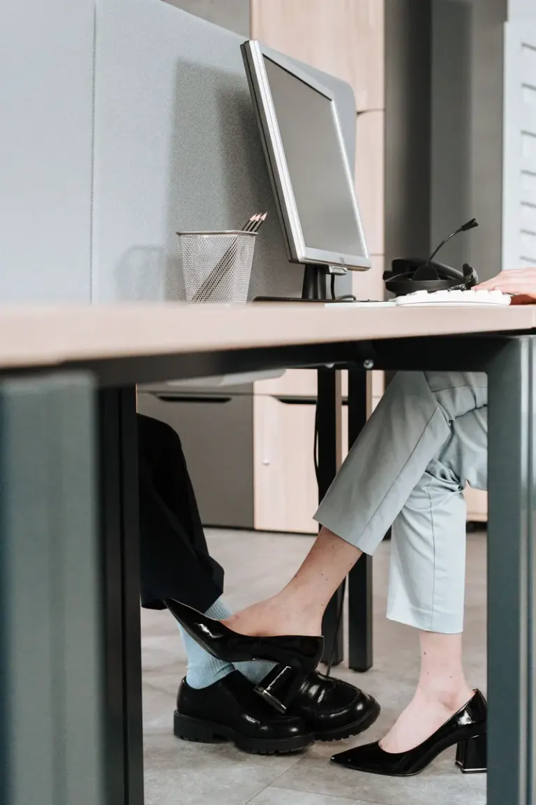 A playful moment between colleagues with foot contact under the office desk. Stock Photo