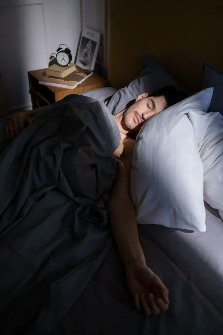 A man sleeps peacefully in a sunlit bedroom, with soft shadows cast on his face. Stock Photo