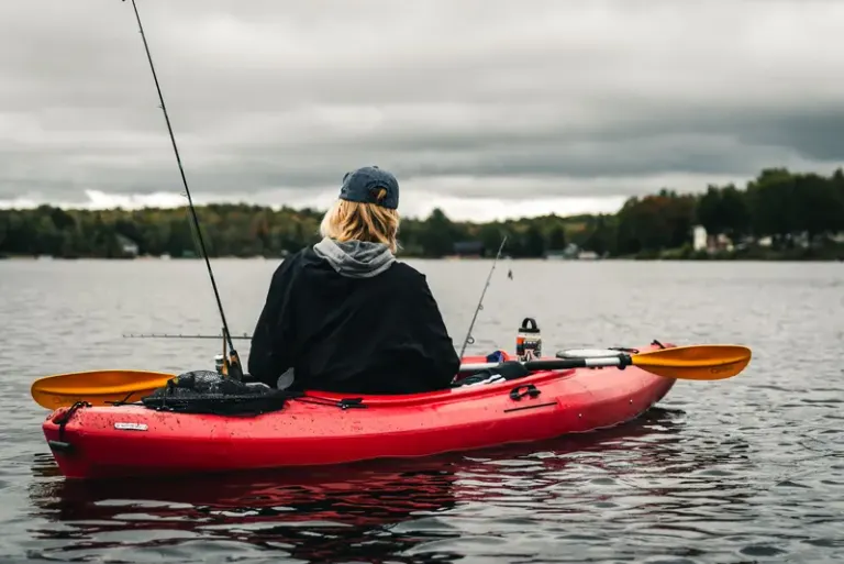 Back view of a person in a red kayak fishing on a tranquil lake with a cloudy sky. Stock Photo