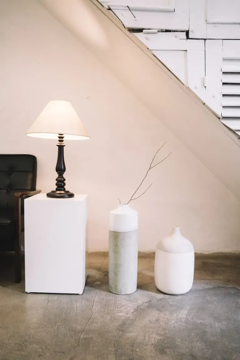 Stylish interior with a minimalist lamp and decorative vases under stairs. Stock Photo