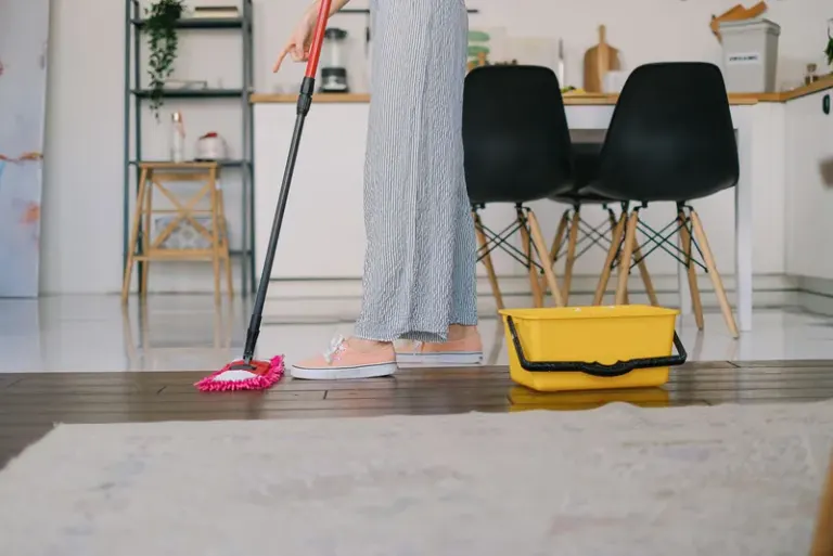 Side view of crop anonymous woman washing parquet with mop against bucket and carpet in house Stock Photo