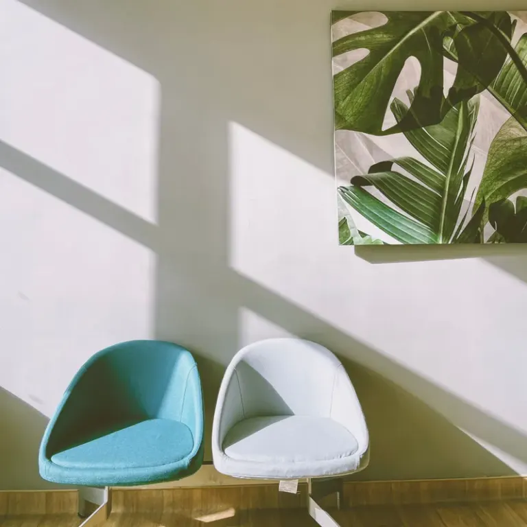 Stylish modern interior featuring two chairs and vibrant leaf artwork on a sunlit wall. Stock Photo
