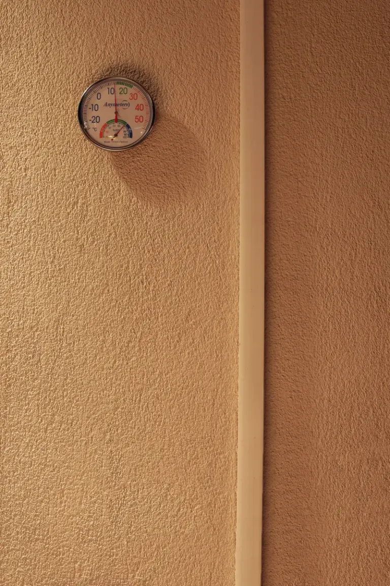 A minimalist indoor scene featuring a hygrometer mounted on a textured wall, indicating temperature and humidity. Stock Photo