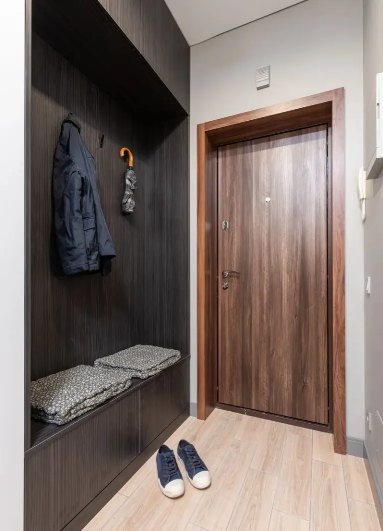 Modern light apartment interior with wooden wardrobe with jacket near umbrella and textile on shelf near sneakers and door Stock Photo