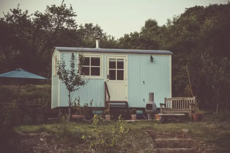A cozy and rustic tiny house in the countryside with outdoor seating and lush greenery. Stock Photo