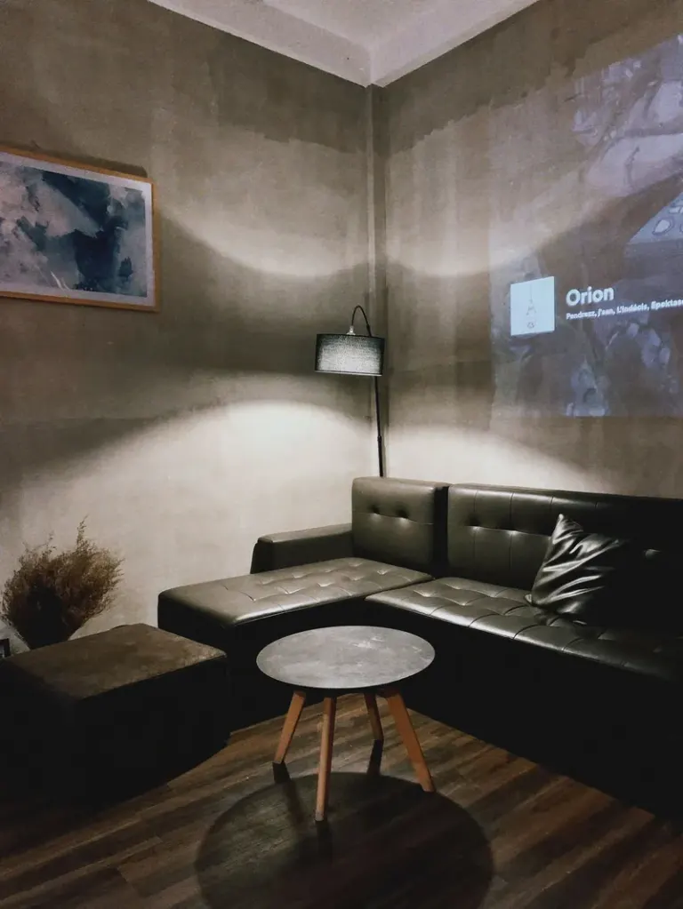 Interior of modern apartment with comfortable leather sofa placed in corner near wall with projection and round table near sofa lit by floor lamp Stock Photo