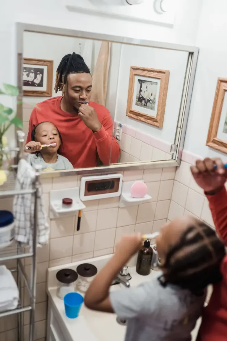 A joyful father and child brushing teeth together in a home bathroom mirror reflection. Stock Photo