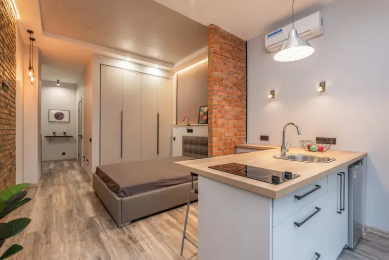 Miniature kitchen with modern appliances and bedroom behind brick partition in small loft style apartment Stock Photo