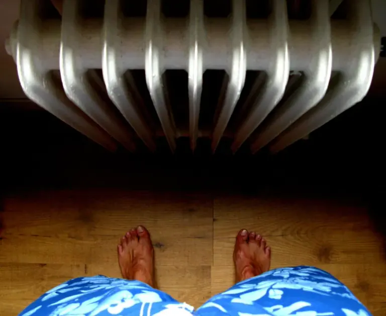 A unique perspective from above showing bare feet standing on wooden floor near a radiator. Stock Photo