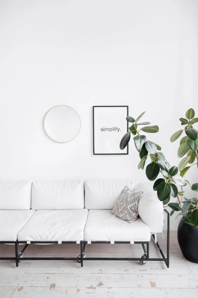 A bright minimalist living room featuring a white sofa, indoor plant, and wall decor creating a clean and serene space. Stock Photo