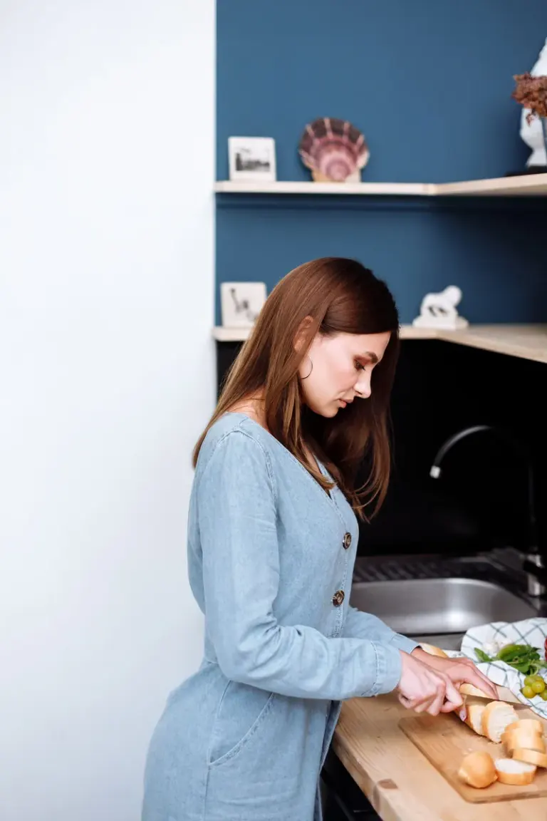 Side view of a woman slicing a baguette on a cutting board in a stylish indoor kitchen. Stock Photo