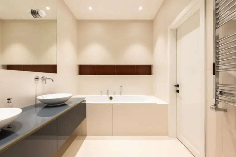 Interior of modern bathroom with sinks on cabinet near tap and mirror near bath and door Stock Photo