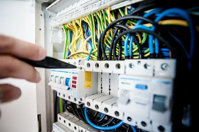 Hand of electrician working on a circuit breaker panel with colorful wires, ensuring safe electrical connections. Stock Photo