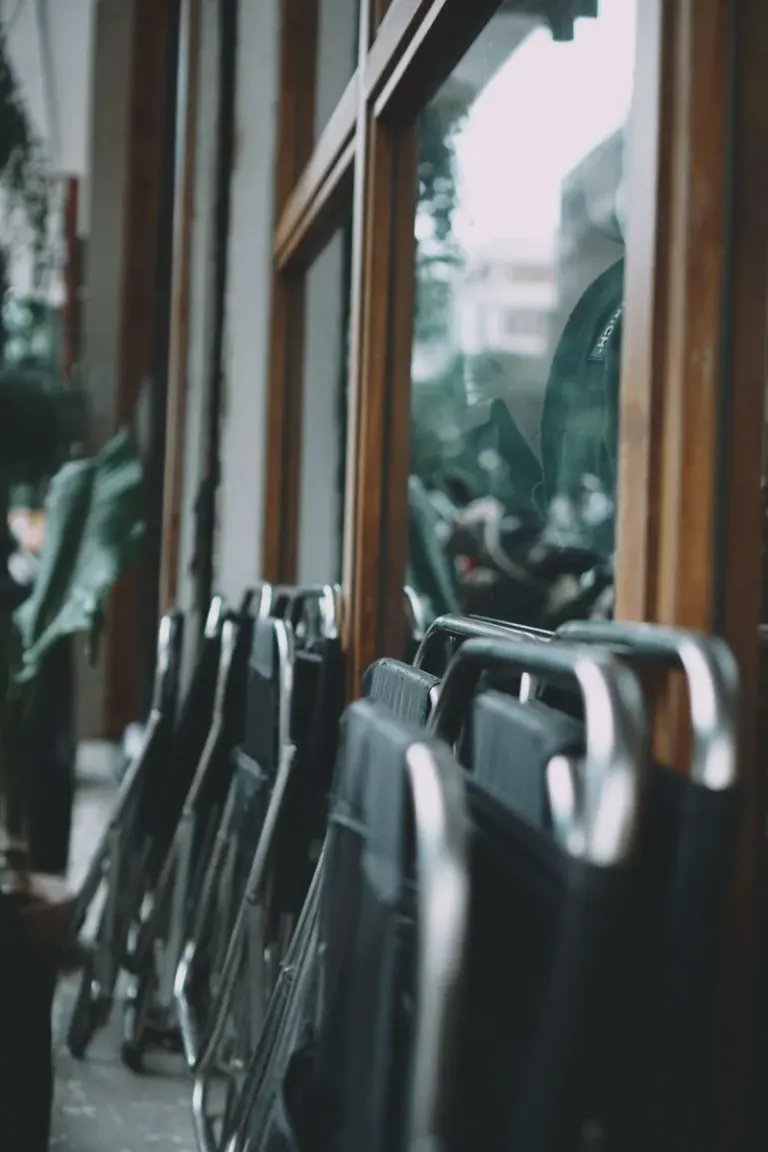 A row of folded chairs leaning against a glass window façade, creating a reflective urban scene. Stock Photo