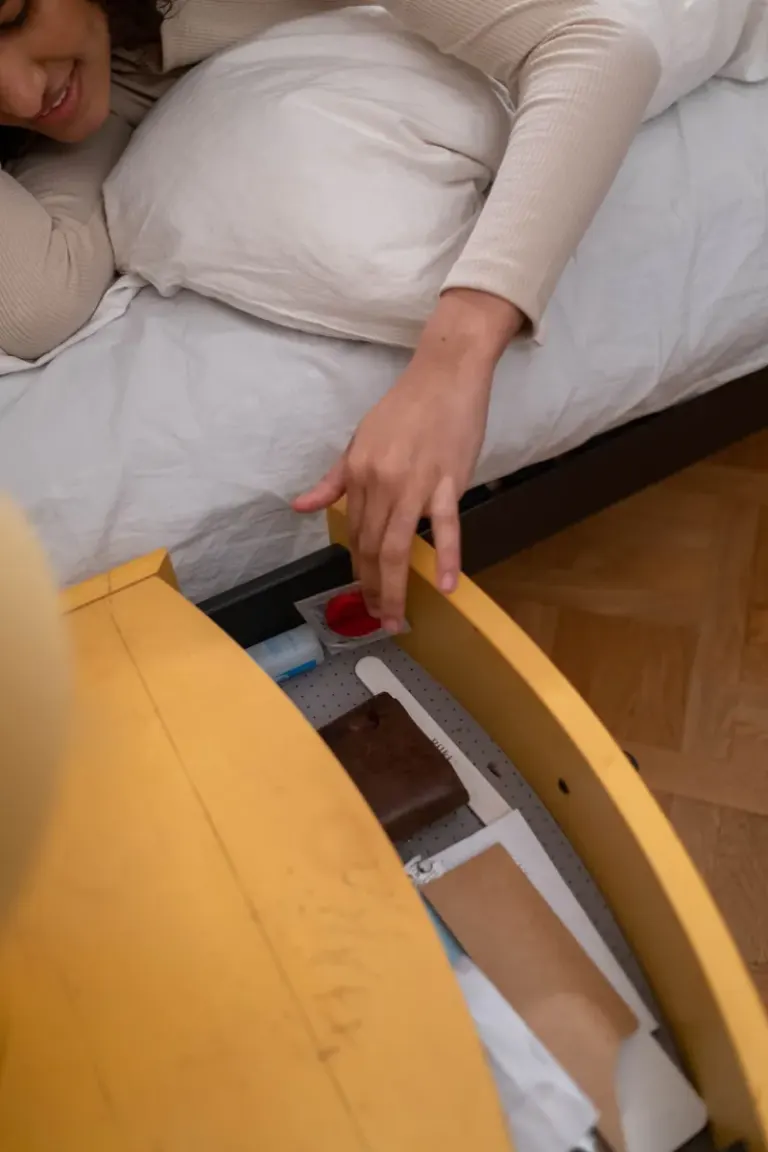 A woman smiling while reaching for a protected item in a bedside drawer. Stock Photo