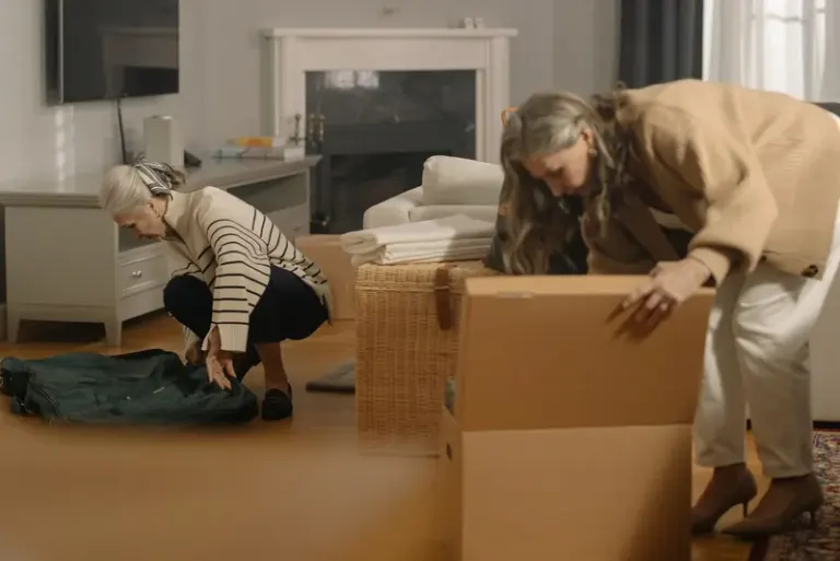 Two senior women packing belongings in boxes, preparing for a move in a cozy living room. Stock Photo