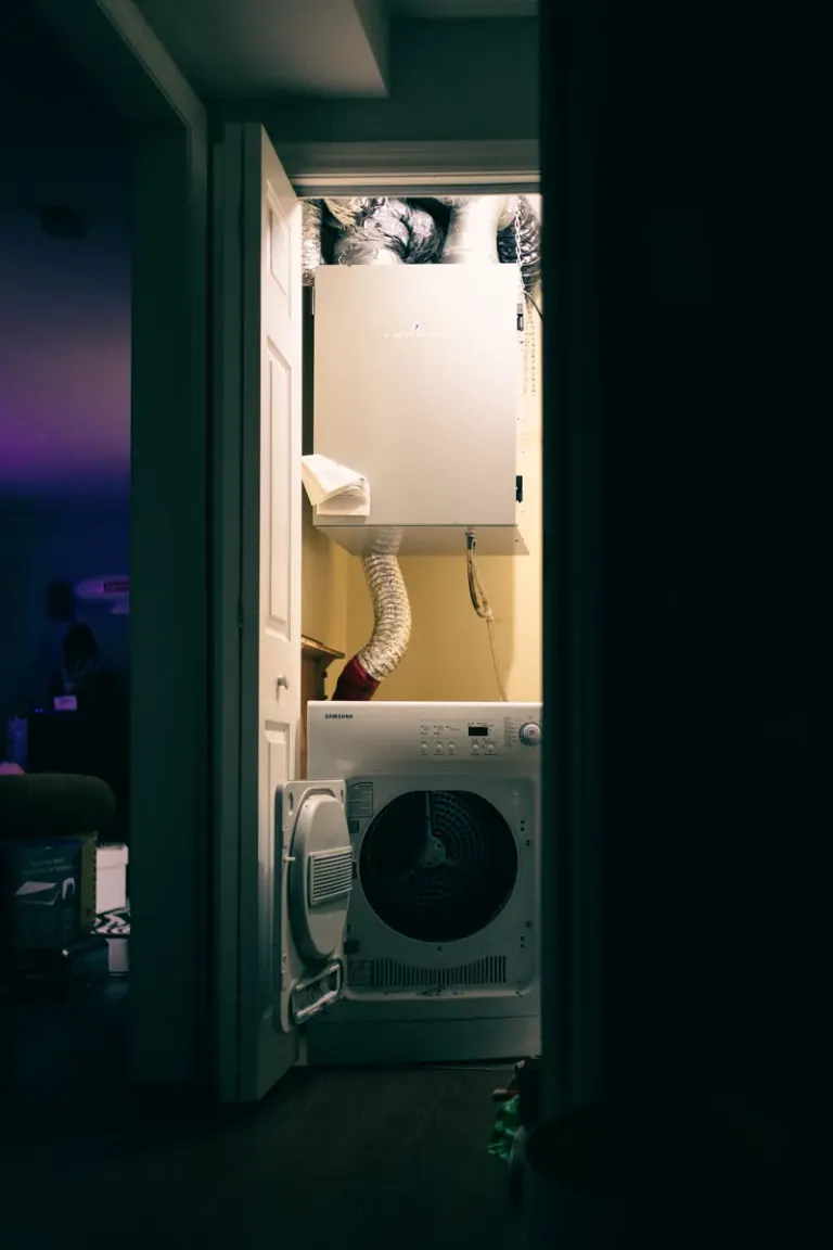 A cozy laundry closet with a dryer and ventilation system, illuminated in low light from indoors. Stock Photo