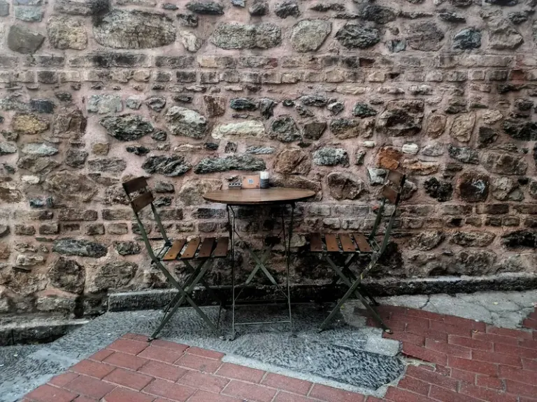 Cozy outdoor bistro with wooden chairs and a table against a rustic stone wall. Stock Photo