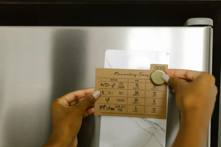Hands placing a marinating timer card on a fridge with a magnet, featuring cooking times for various proteins. Stock Photo