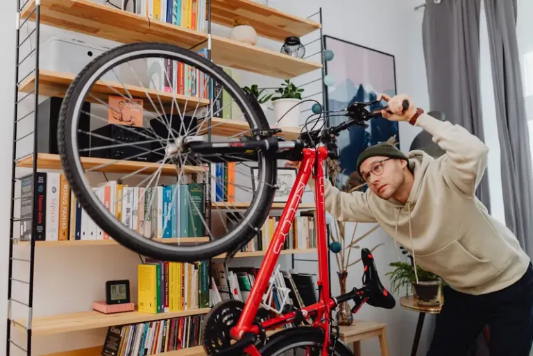 A man in a hoodie adjusts a bicycle indoors in front of a bookshelf. Stock Photo