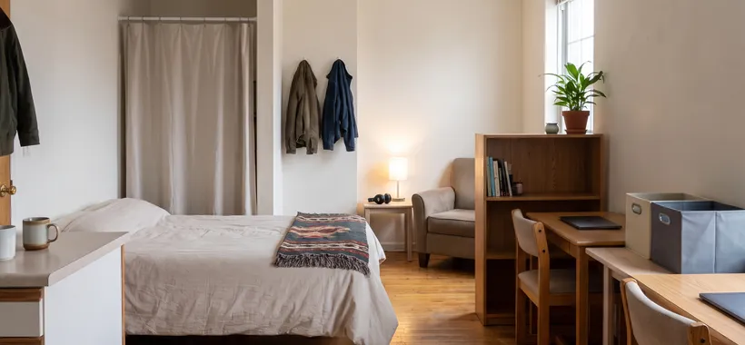 A bright studio apartment arranged for two people, with a bed, two desks and a curtain marking a private corner