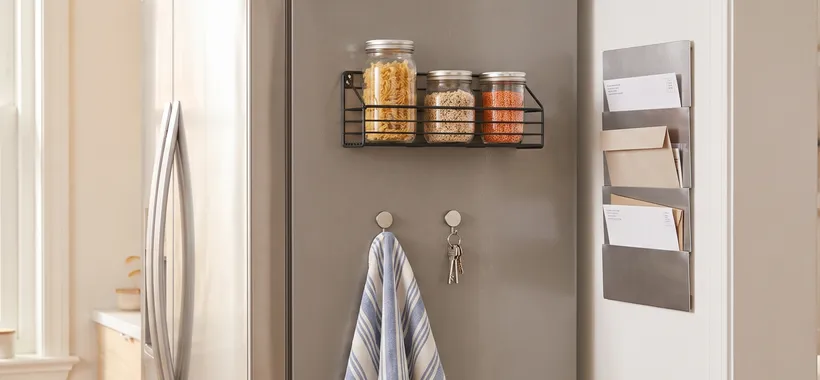 A bright small kitchen with magnetic shelves and hooks on a fridge side holding jars, towels, and keys