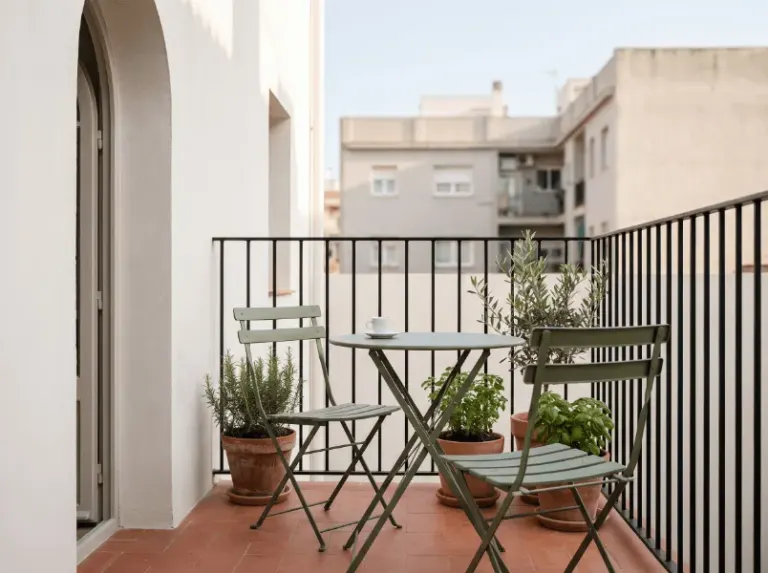 A small furnished balcony with folding chairs, a table, and potted herbs